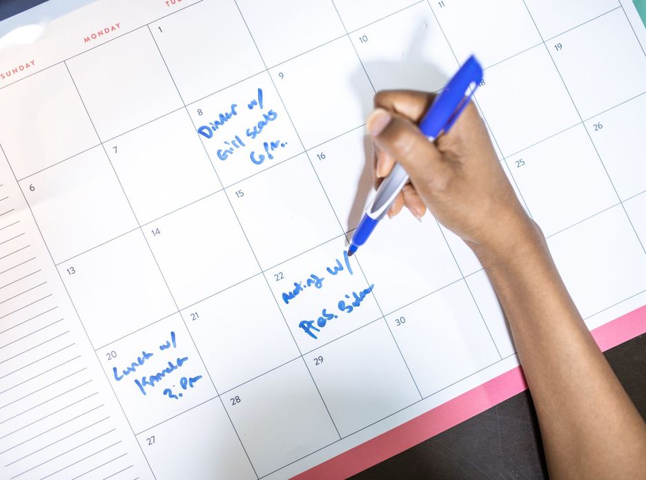 Person writing appointments on a calendar with a blue pen