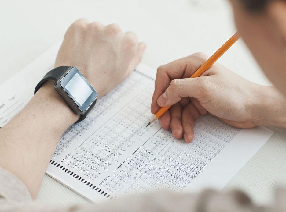 Close-up of a student writing answers on a test sheet with a pencil and smartwatch