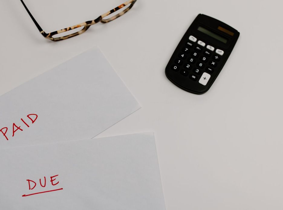 Top view of financial papers labeled 'Paid' and 'Due' beside a calculator and glasses