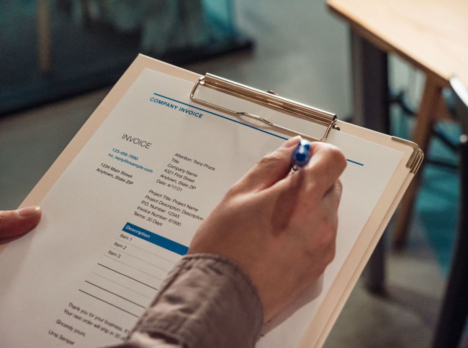 Person's hand holding a company invoice on a clipboard with a pen