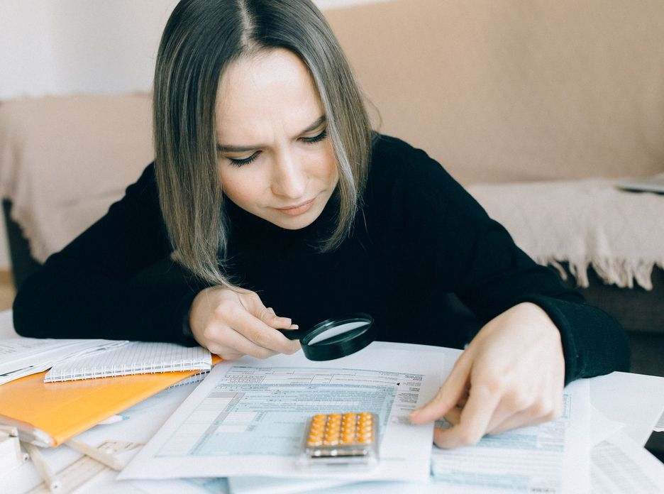 A focused young woman examines documents with a magnifying glass