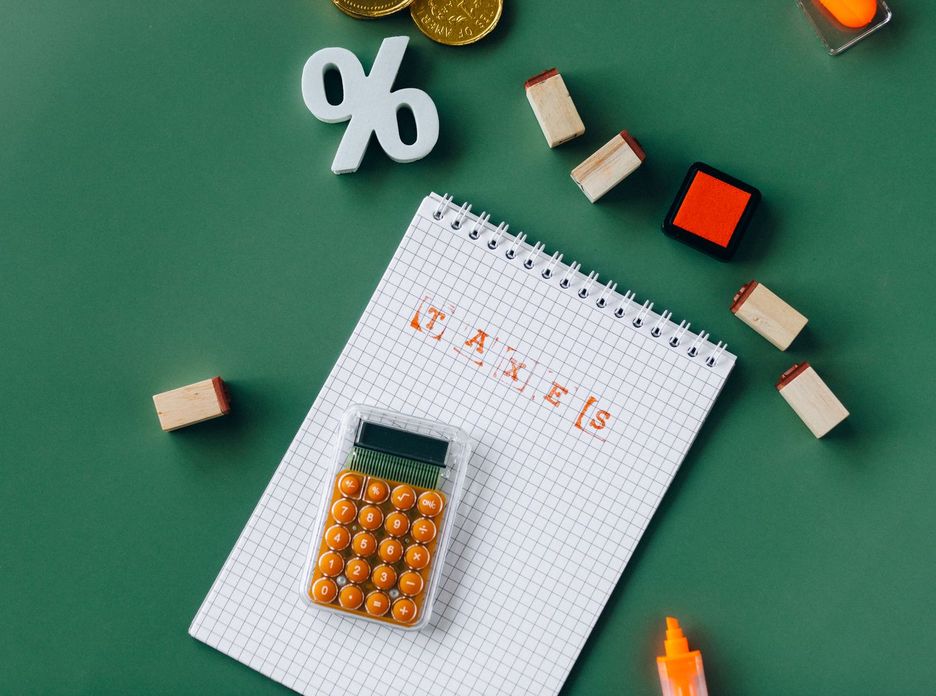 Flat lay of tax essentials with calculator, notebook, and stamps on a green background