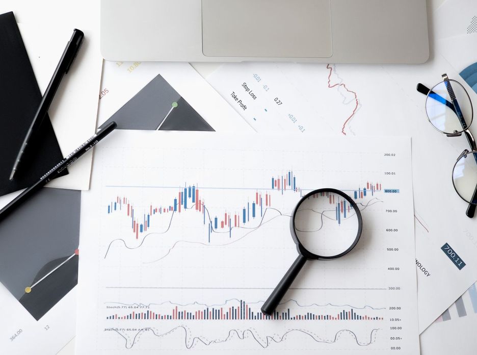 Flat lay of stock market analysis documents with magnifying glass, pens, and glasses