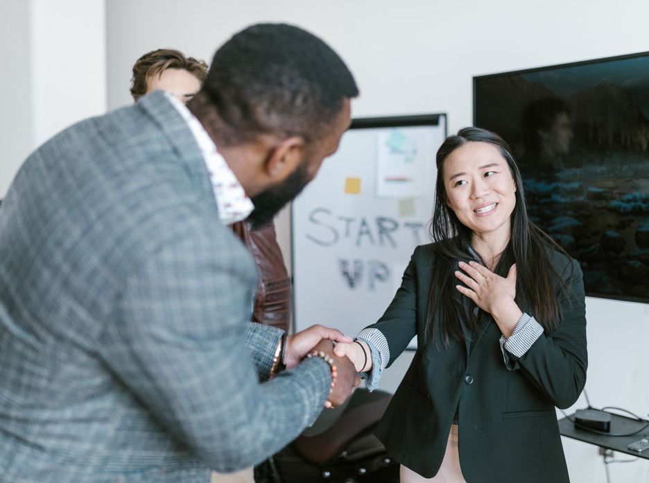 A diverse business team in formal attire exchanging a handshake in a modern office setting