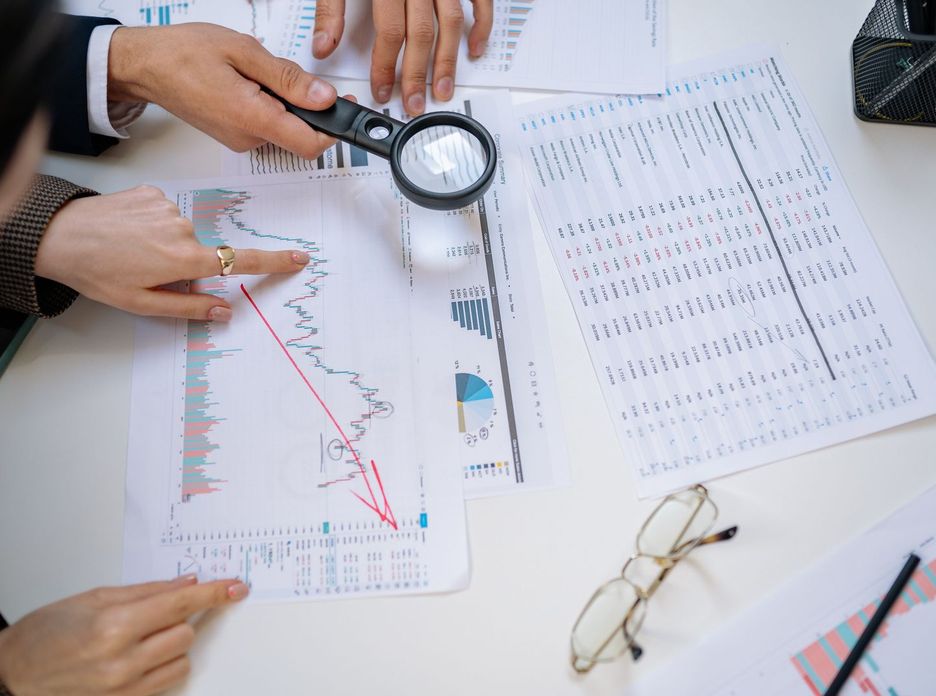 Business professionals examining financial documents with magnifying glass for detailed analysis