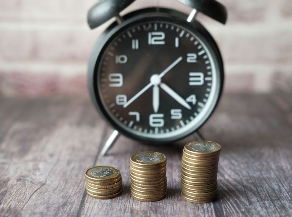Stacked coins and a classic alarm clock symbolize the value of time and money