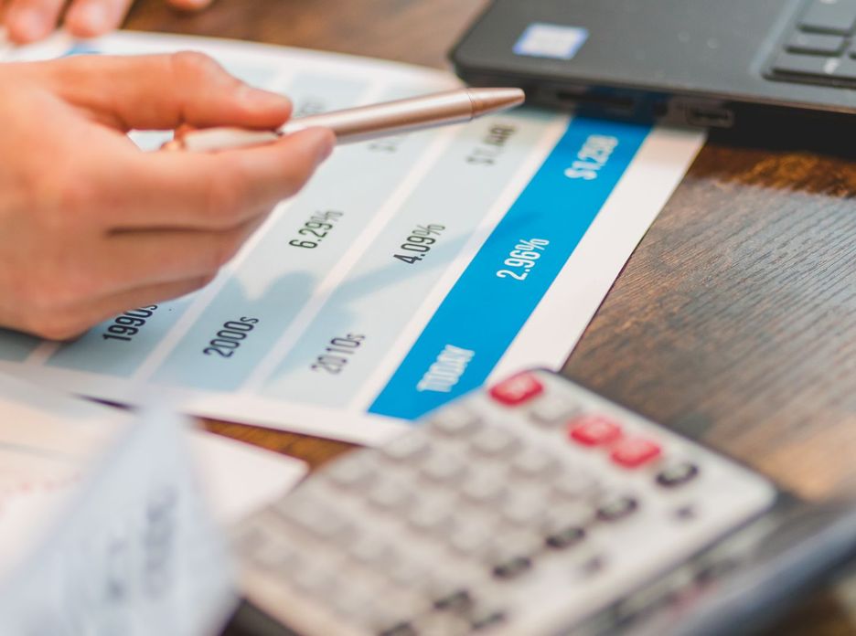 Close-up of a hand using a ballpen and calculator to analyze interest rates on a chart