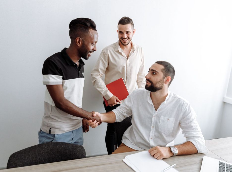 Three men in an office setting engaging in a friendly handshake
