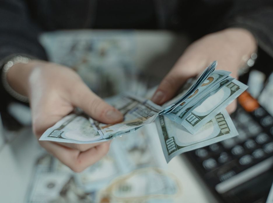 Close-up of hands counting hundred dollar bills with a calculator in the background