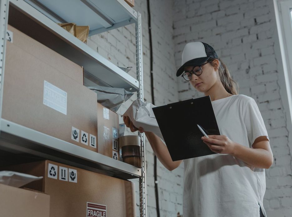 Warehouse worker organizing packages on shelf with clipboard