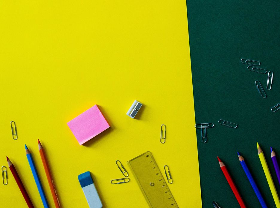 Top view of colorful school supplies on a vibrant yellow and green background