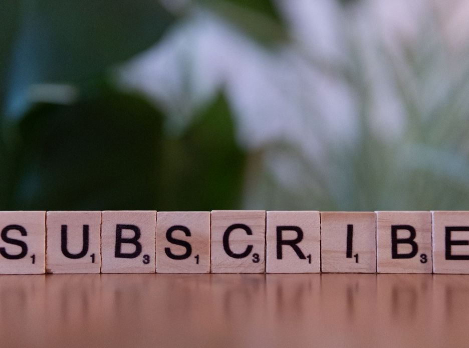 Close-up of the word 'SUBSCRIBE' spelled with wooden letter tiles on a table