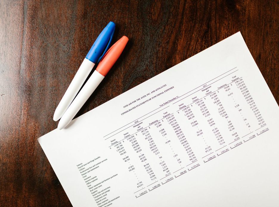 A financial statement on a wooden desk with colorful pens
