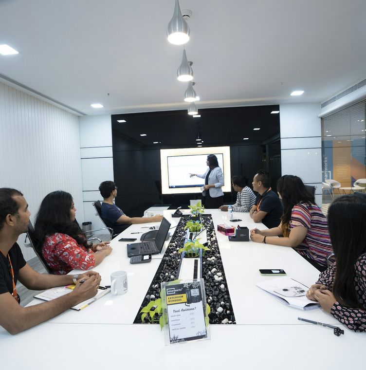 A team in an Indian office at a long meeting table, watching a colleague present on a screen