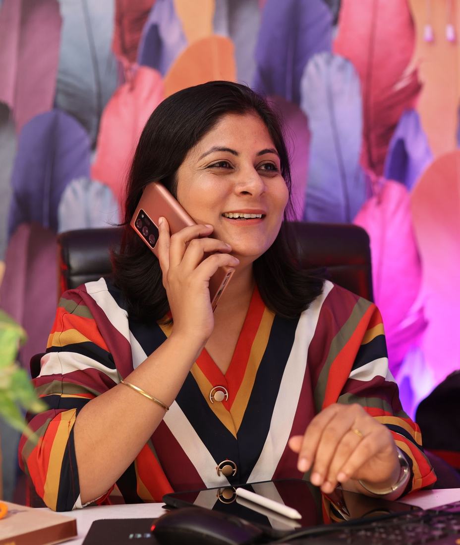 A smiling woman in a striped top on a phone call at her desk