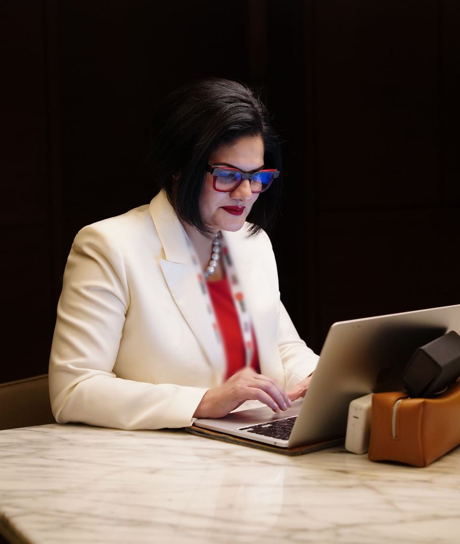A woman in a white blazer working on a laptop at a marble desk
