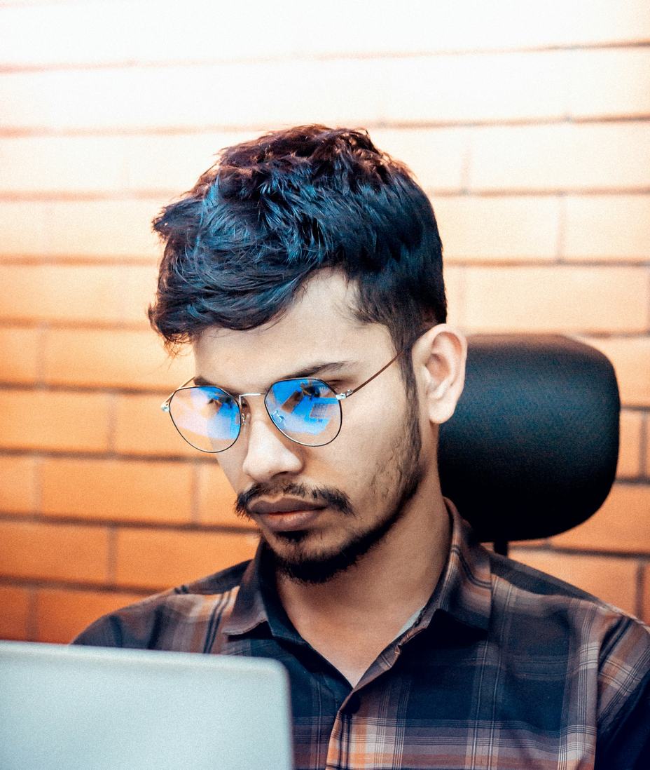 A young man in glasses and a checked shirt looking at his laptop