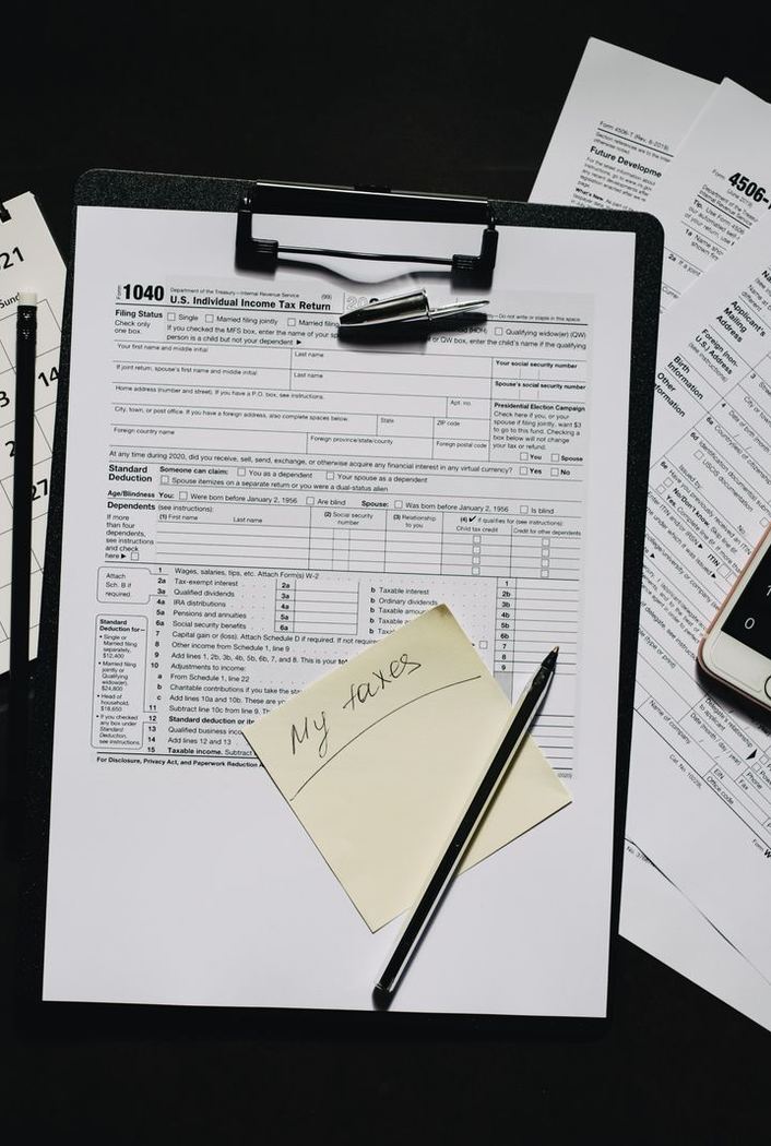 Clipboard with a tax form, a sticky note, a phone calculator and a desk calendar on a dark table